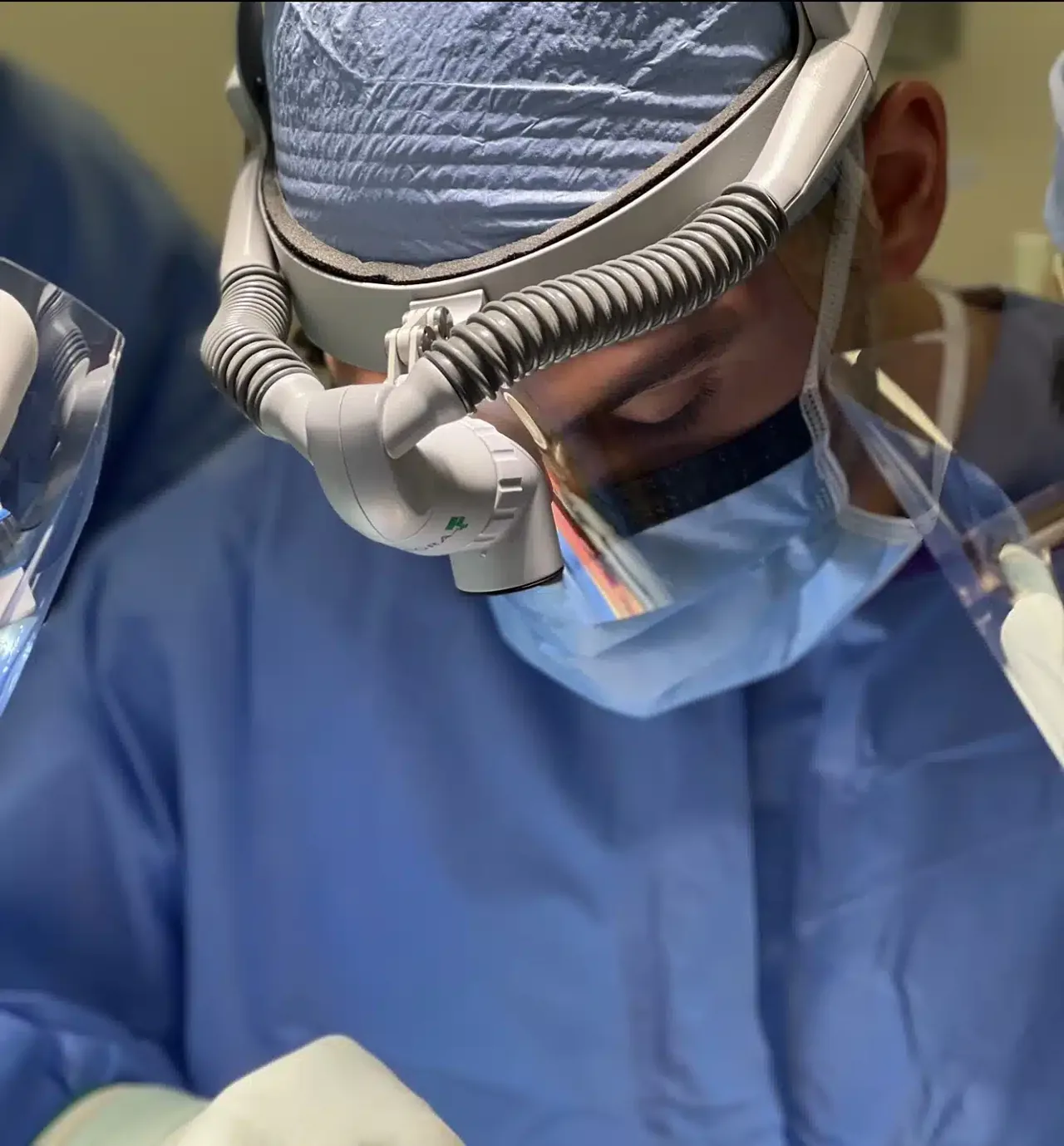 Dr. Chad M. Curtis, DDS, in surgery wearing a gown, mask, face shield, and surgical loupes